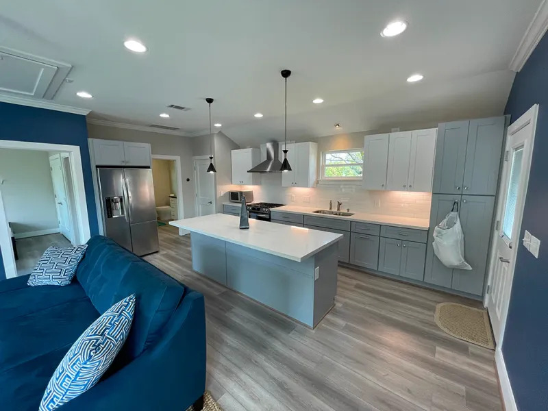Modern open-concept kitchen with gray cabinets, white island, pendant lighting, and wood-look flooring
